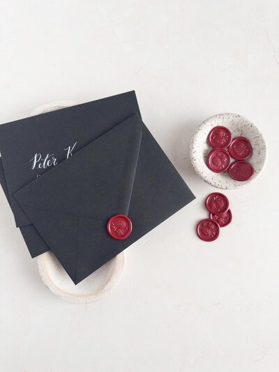 DC calligrapher and wedding stationery designer assembling custom wedding invitation black envelopes with rich red wax seals