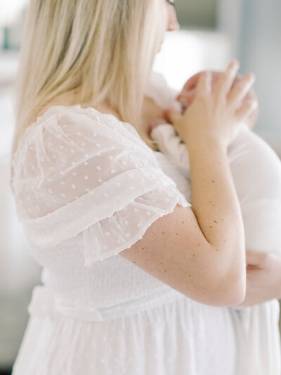 Blonde mother in a white, sheer, polka dotted dress puts pacifier into her newborn son's mouth at their Little Rock home