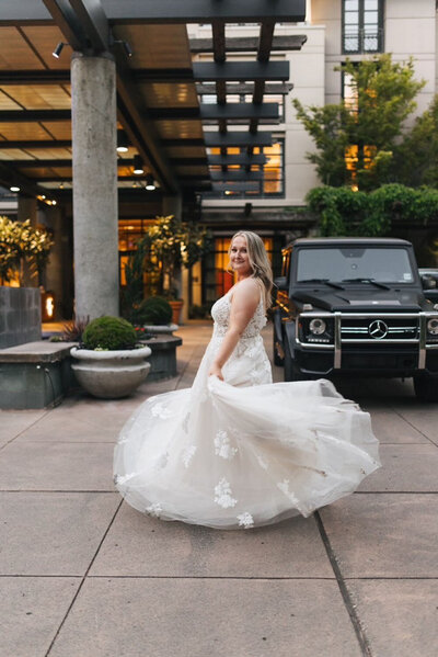 A bride twirling in her gown, standing confidently beside a luxury car