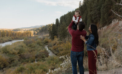A husband and wife facing away from the camera. The husband is holding their baby up above their heads.