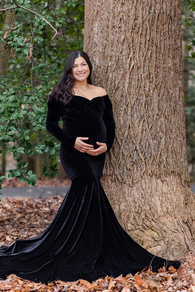 A momma-to-be holding her pregnant belly and leaning against a tree at a park in Burke, Virginia.