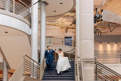 Bride and Groom hug and laugh surrounded by their bridal party. Bride has a flower crown and groom is in  a black tux. Anna Brace, a wedding photographer omaha nebraska