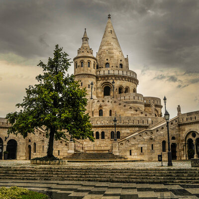 Historic Fisherman’s Bastion in Budapest, featuring rounded towers, stairways, and dramatic cloudy skies.