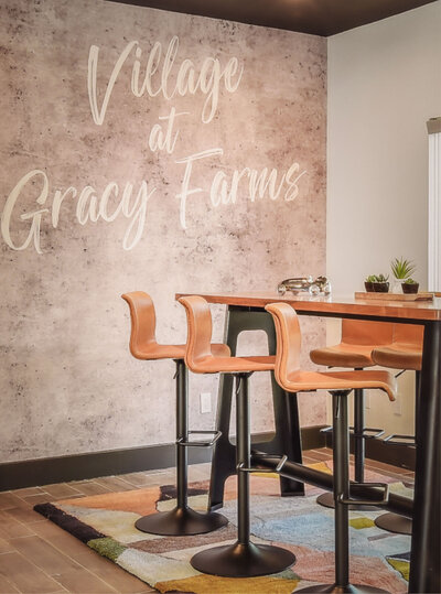 Contemporary seating area at Village at Gracy Farms featuring high-top stools, a modern rug, and a textured accent wall.
