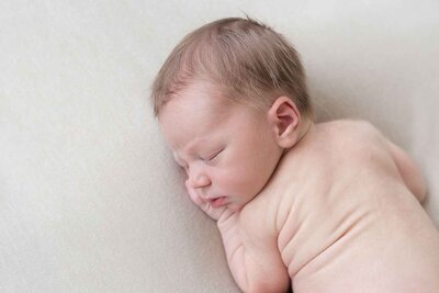 Newborn shoot aan huis met een zachte crèmekleurige achtergrond.