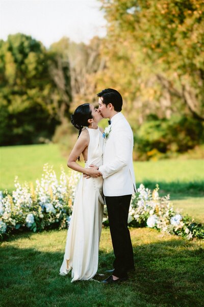 Bride in a long elegant dress sitting in front of a table decorated with lots of floral centerpieces