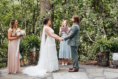bride and groom holding hands while standing under trees