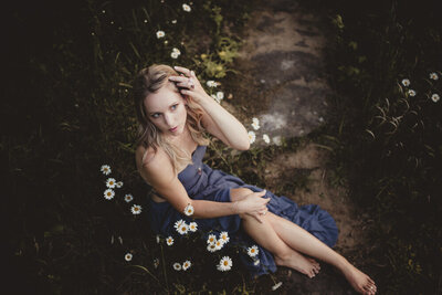 Caroline sitting among white flowers, embodying softness, gratitude, and grounded energy.