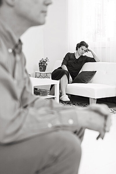 A woman sitting on a couch with another person sitting in the front of the room