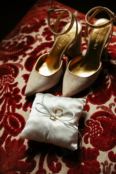 A close-up of the wedding rings and the bride's luxurious shoes, beautifully displayed with a draped backdrop, capturing the sophisticated charm of the wedding accessories
