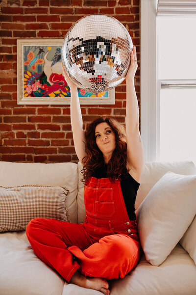 A woman sitting on a couch holding up a disco ball.