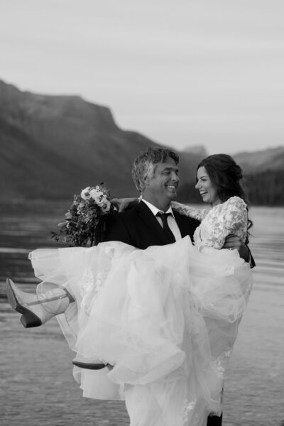 Black and white photo of groom lifting his smiling bride during a joyful wedding moment.