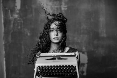 Portrait of woman with curly hair holding a vintage typewriter posing for a portrait, photo is in black and white