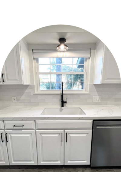 A kitchen with new white cabinets and countertops and black trim. The focus is the sink with a window above it.