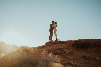man and woman standing on large red rock while kissing