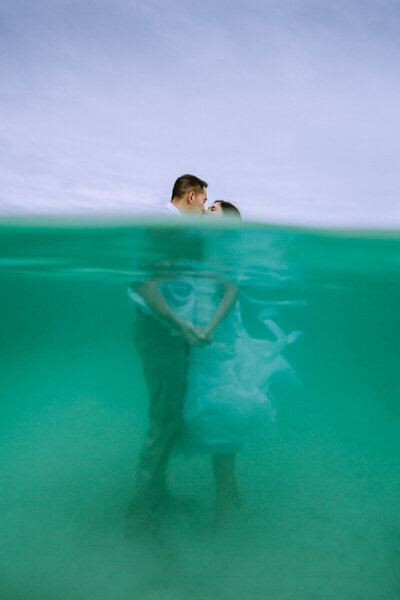 couple kissing underwater with half over half under