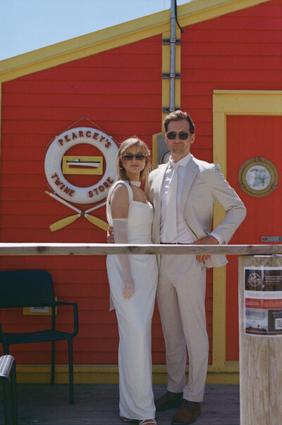 film photo of a couple standing in front of a bright red fishing shed