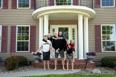 Family of six in front of their house giving each other piggy back rides.