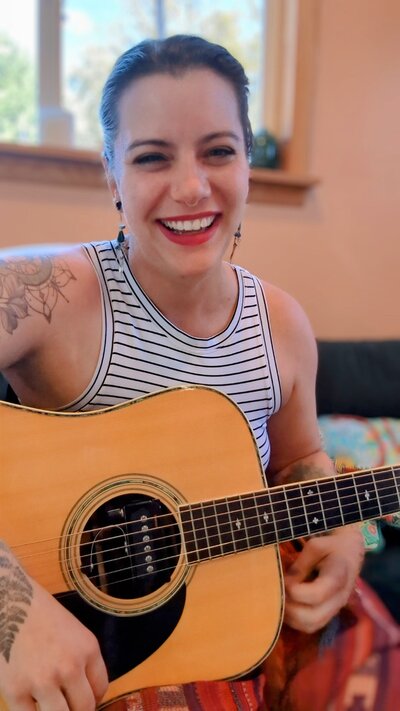 Julie Pokorny, craniosacral therapist and integrative health coach, smiling while playing guitar in her Maryland studio.