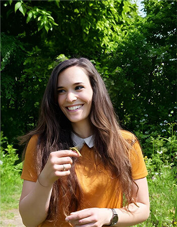 Delphine, souriante, en extérieur, montrant une libellule posée au bout de son doigt. Interlocutrice sur le projet d'identité visuelle de la maison des libellules.