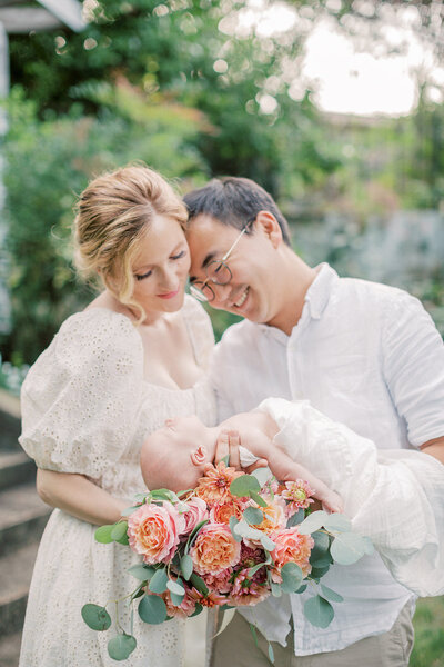 New parents stand in a garden holding their newborn baby with roses photographed by Washington DC Newborn Photographer Marie Elizabeth Photography