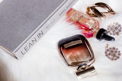 Bottles of perfume laying next to a fashion book on a white fur background