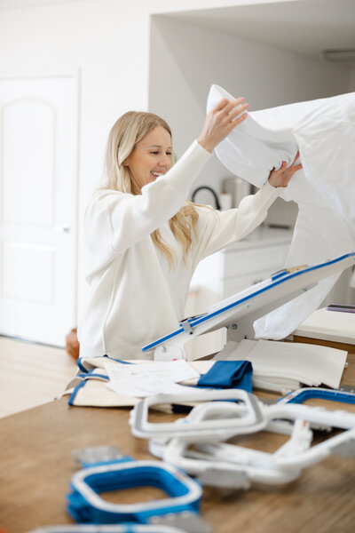 Blonde woman working with fabric and embroidery equipment in a bright studio. Photograph by Yucaipa branding photographer Kaitlyn Dawn Photography.