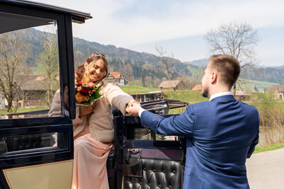 Der liebevolle Bräutigam reicht seiner Braut die Hand und hilft ihr aus der eleganten Kutsche von Kutschenfahrten Scherrer, eine Geste voller Zärtlichkeit und Fürsorglichkeit.