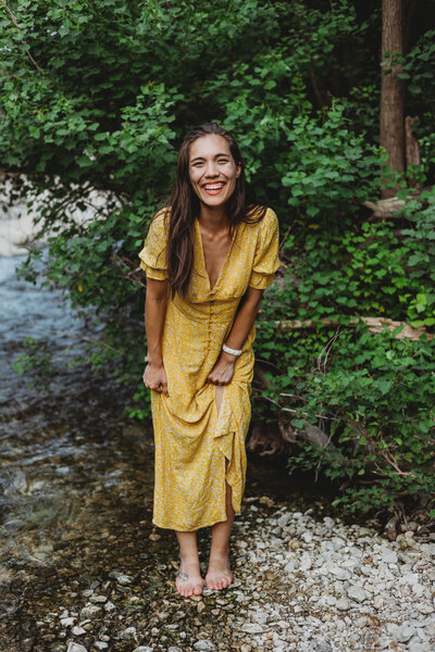 Jennie, owner and designer at coulter creative co standing in nature in front of tree, smiling with a yellow dress