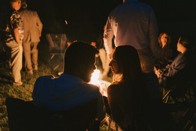 Candid photo of couple sitting by a campfire at a wedding