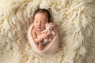 newborn girl in pink wrap and holding teddy bear