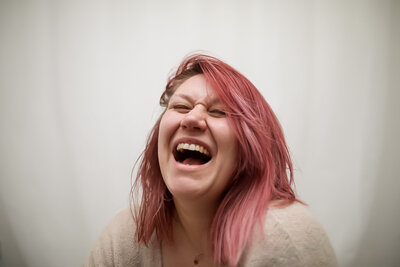 woman with pink hair laughing with a wide mouth in a  full on laugh