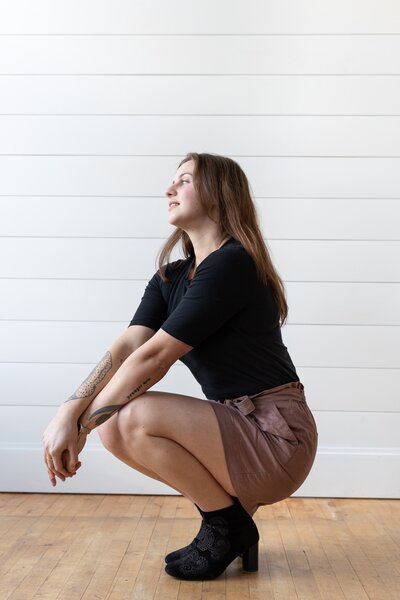 Local website designer who creates websites for small business owners is posing in a crouched position for photoshoot.