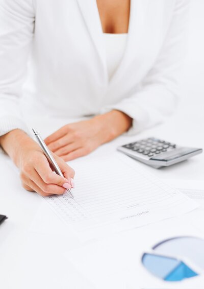 Image  showing the chest and hands of a woman dressed in a white business suit working on her bookkeeping.