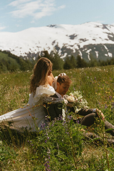 Alaska elopement photos of bride and groom sitting in grass