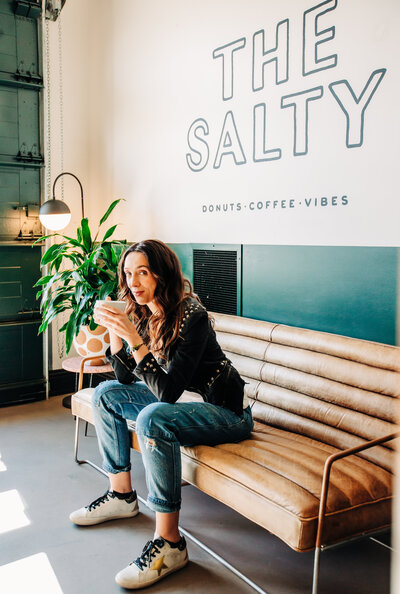 Headshot of photographer and videographer Maria drinking coffee in a cafe looking at the camera