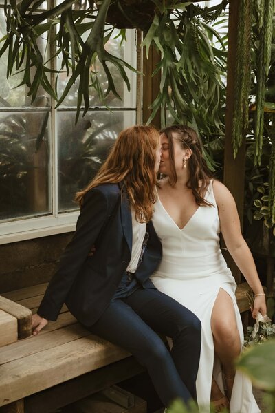 Two brides smooch at the Volunteer Park Conservatory in Seattle, Washington