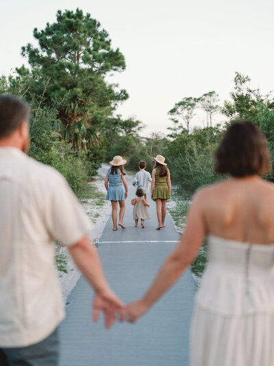 Courtney Leigh and her husband holding hands blurry in the foreground with her kids walking down a boardwalk in focus in the background
