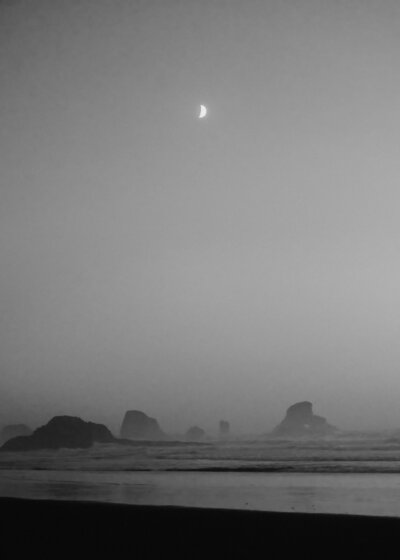 At the end of their Oregon coast elopement, a crescent moon shines over a moody beach