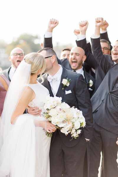 Bride and groom kissing with groomsmen cheering