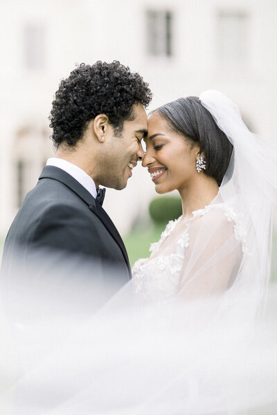 a bride and groom embracing while wrapped in a wedding veil