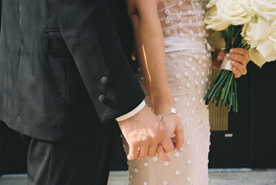 Bride and groom interlock fingers displaying close up details of the bride's beaded gown