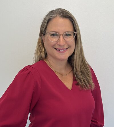 woman with blonde hair and glasses smiling while looking at the camera