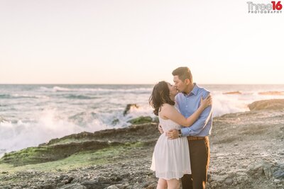 Engaged couple share a romantic kiss on the rocky part of Victoria Beach in Laguna Beach