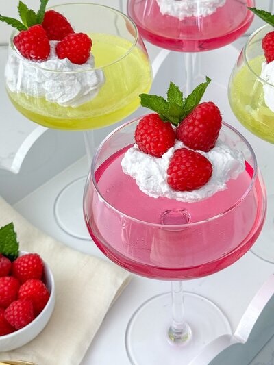 Coupe glasses of lemon and watermelon sugar-free jello, topped with whipped cream, berries and mint.