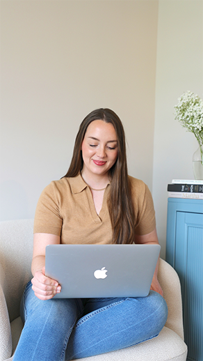 A woman seated on a chair, working on a laptop with a focused expression.