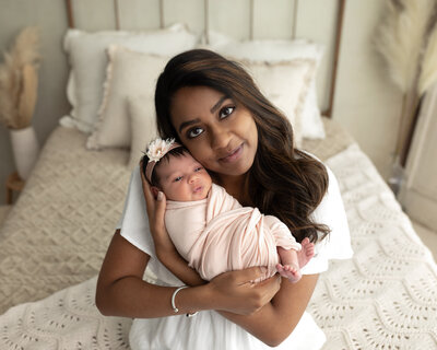 mom holding newborn baby girl wrapped in pink for studio newborn portraits
