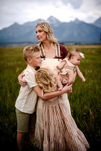 Mother holding her three children closely in a Jackson, WY field. 