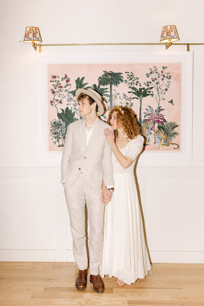 A modern wedding portrait of a couple inside Common House Richmond, standing in front of a warm, art-filled backdrop. The bride wears a soft, romantic dress while the groom is in a light linen suit—perfectly showcasing the modern, design-forward aesthetic of this Richmond, VA wedding venue.