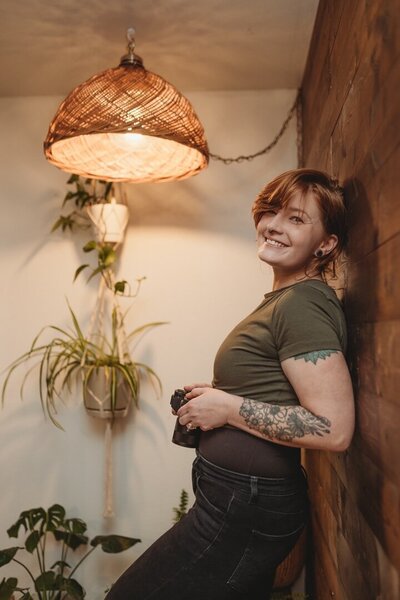 Cherish standing with her back against the wall, holding camera, looking at camera